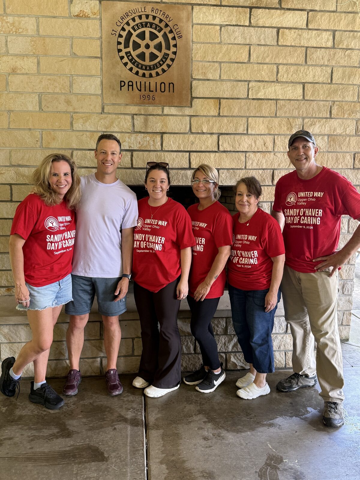 The Goodman Properties team in United Way Day of Caring shirts beneath the St. Clairsville Rotary Club Pavilion plaque at Memorial Park